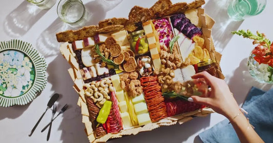 Affordable charcuterie box with assorted cheeses, meats, crackers, and nuts served on a bright casual table setup.