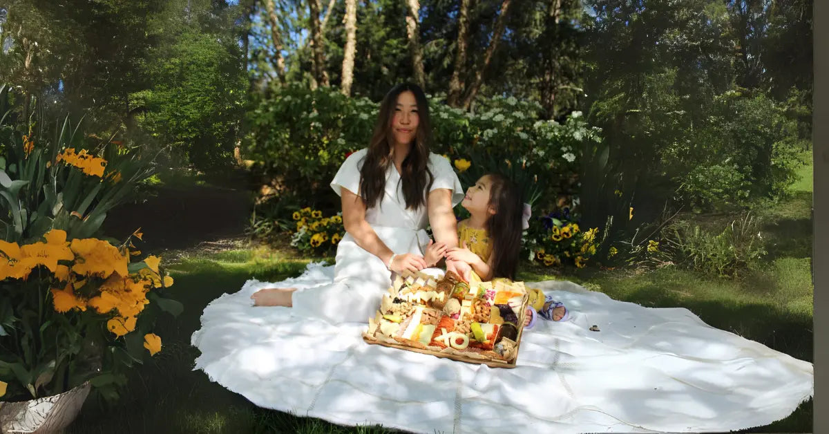 how to style a cheese board with fresh flowers, mixed cheeses, meats, and fruit on a white picnic blanket