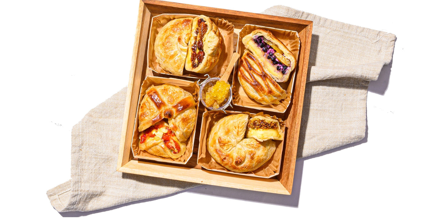 Baked brie board featuring assorted flaky pastry-wrapped brie with sweet and savory fillings in a wooden tray.