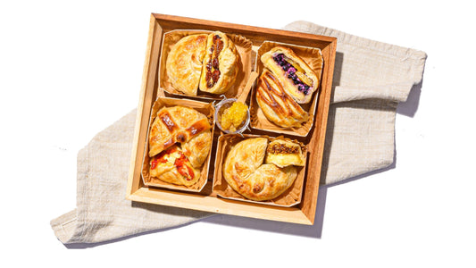 Baked brie board featuring assorted flaky pastry-wrapped brie with sweet and savory fillings in a wooden tray.