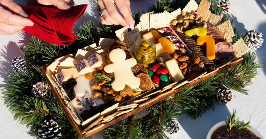 Christmas charcuterie board with a gingerbread man cheese cutout, nestled in pine branches and pinecones on a holiday table.
