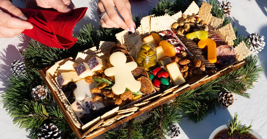 Christmas grazing board with gingerbread-shaped cheese, festive meats, olives, crackers, and nuts surrounded by pinecones and greenery