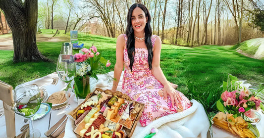 Breakfast charcuterie board set up outdoors with a woman in a floral dress enjoying a morning picnic in the park.
