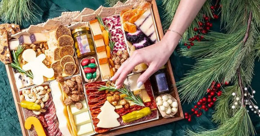 Holiday charcuterie board with festive cheeses, nuts, and meats, decorated with pine branches and red berries