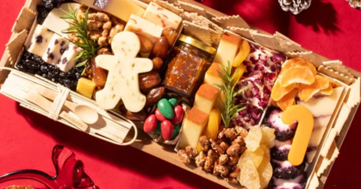 Festive charcuterie board with holiday-themed cheeses, nuts, dried fruits, and treats on a red tablecloth