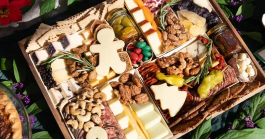 Festive charcuterie board featuring cheeses shaped like a gingerbread man and tree, meats, nuts, & holiday treats