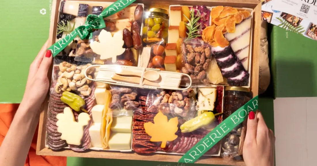 Thanksgiving charcuterie gift box with leaf-shaped cheeses, meats, nuts, and festive packaging featuring green ribbon