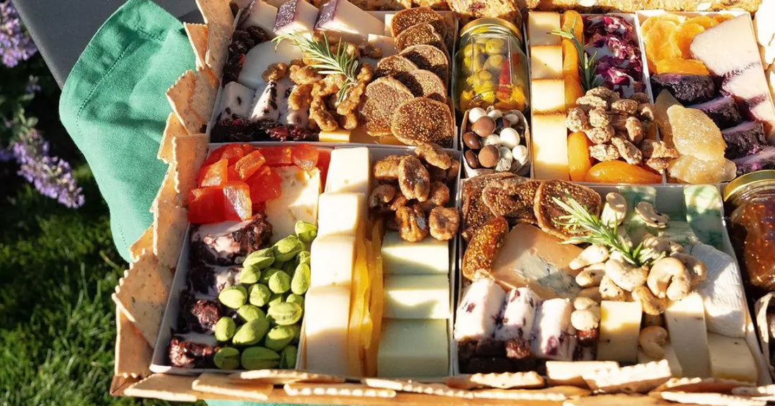 Charcuterie board with assorted cheeses, dried fruits, nuts, figs, and crackers displayed outdoors with a green napkin