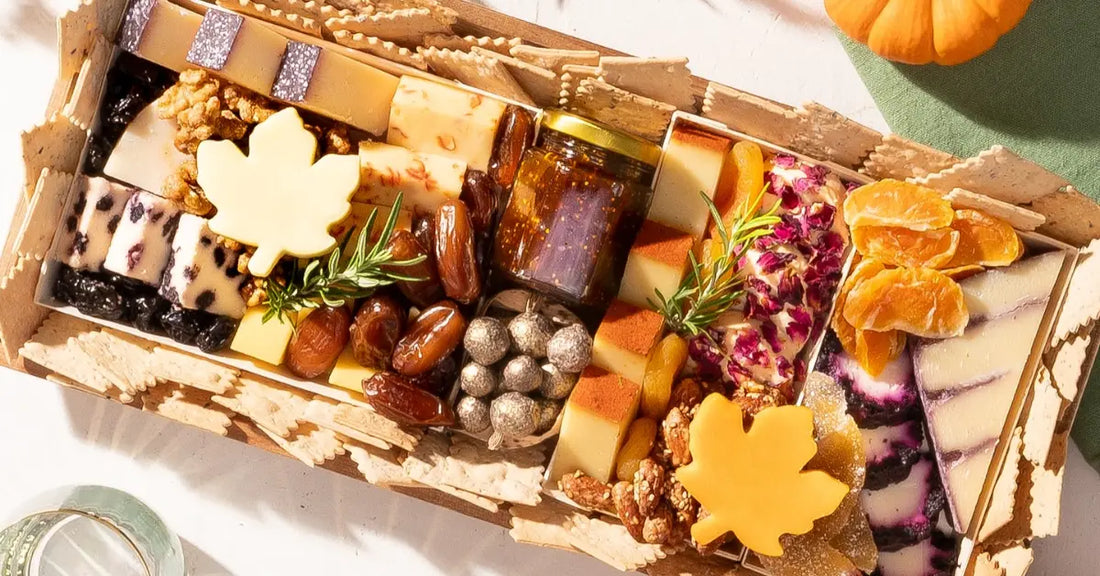 Close-up of a charcuterie board featuring assorted cheeses, dried fruits, nuts, and a decorative autumn leaf cheese cutout