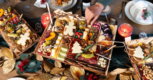 Holiday charcuterie boards with tree-shaped cheeses, candles, and pinecones on a festive table.