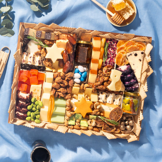 Hanukkah cheese board with Star of David cheeses, nuts, dried fruit, and honey on blue linen.
