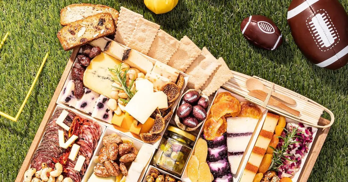 Super Bowl charcuterie spread featuring assorted cheeses, meats, crackers, and football-themed treats on a grass background