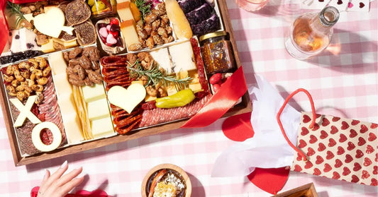 Valentine's Day charcuterie board with heart-shaped cheese, meats, nuts, and sweets styled on a pink gingham picnic setup.