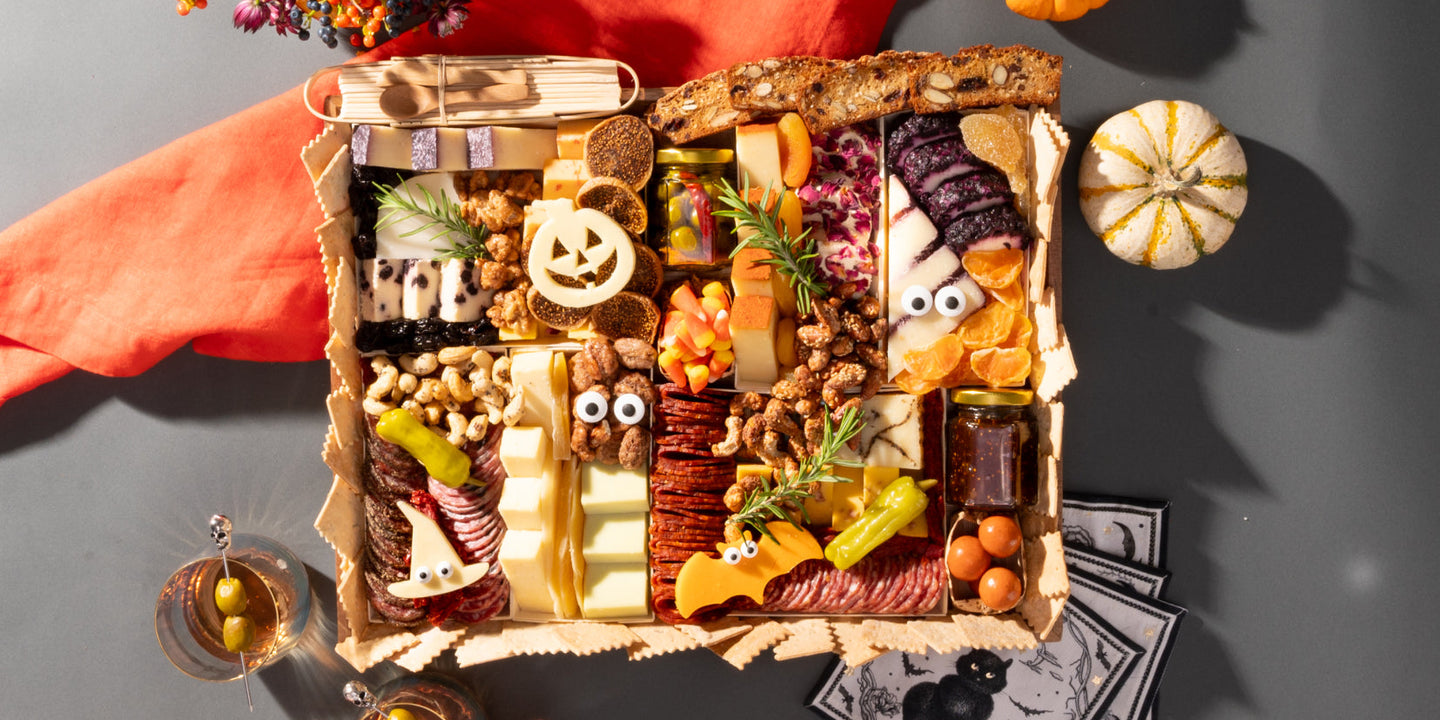 Boarderie's CharBOOterie — a Halloween Cheese and Charcuterie board with a jack-o-lantern cheese, googly-eyed cheese characters, artisan meats, candy corn, fig jam, and a gourmet assortment of artisan cheeses in a reusable acacia wood board
