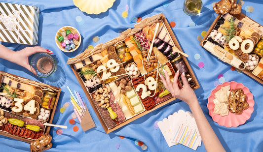 Birthday charcuterie boards topped with number toppers, set on blue linen with confetti and candles.