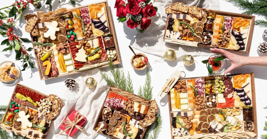 Several Christmas charcuterie boards styled with pine cones, greenery, roses, and a wrapped gift.