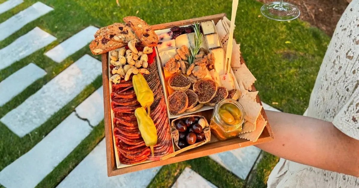 Charcuterie board ideas for football games shown as handheld board with sliced salami, cheeses, nuts, and pickled peppers.