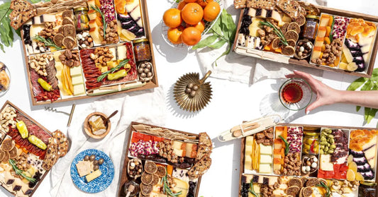 Charcuterie board spreads with cheeses, meats, nuts, and fig jam arranged for a vibrant outdoor gathering with drinks.
