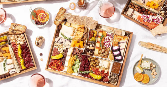 Romantic charcuterie board featuring multiple platters of assorted cheeses, meats, fruits, and snacks for a shared picnic.