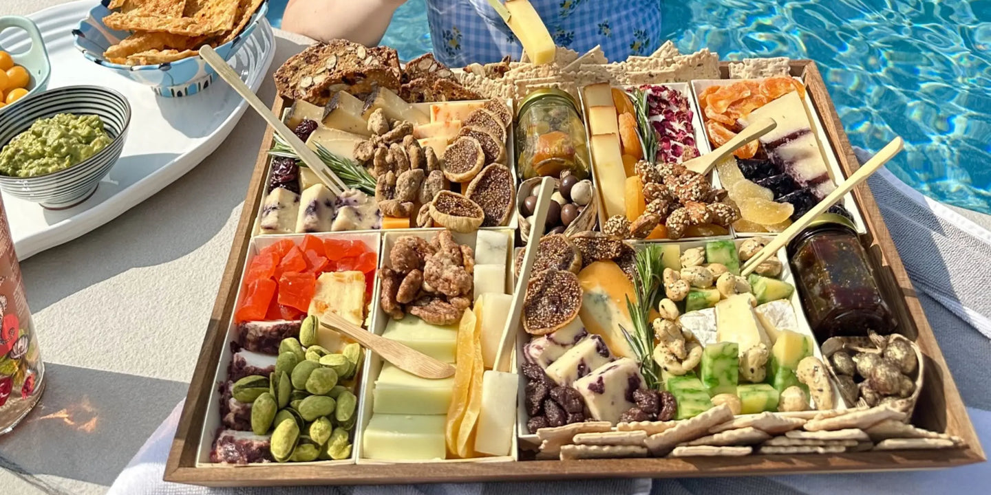 charcuterie tray loaded with cheeses, figs, nuts, dried fruit, and crackers served poolside with guacamole and crackers nearby