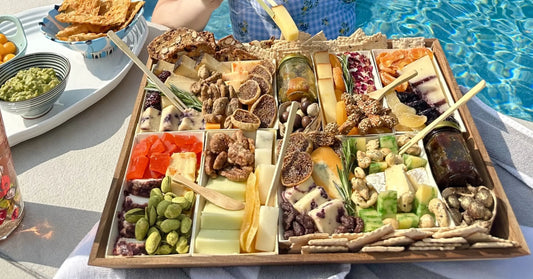 charcuterie tray loaded with cheeses, figs, nuts, dried fruit, and crackers served poolside with guacamole and crackers nearby