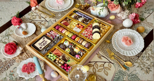 charcuterie tray filled with macarons, truffles, chocolates, and candies displayed on a floral Easter table setting