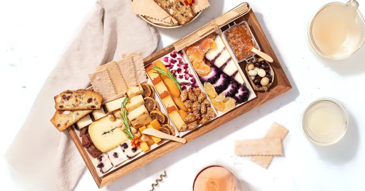 Sympathy charcuterie board with assorted cheeses, fruits, crackers, and spreads on a wooden tray with drinks.