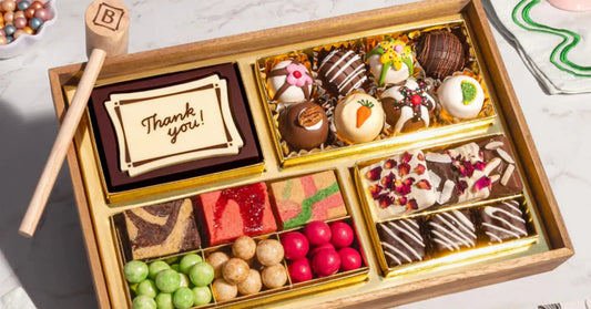 cheese and meat board packed with chocolates, truffles, and brownies in a gold-lined wooden tray with a thank you message