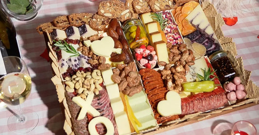 cheese tray board featuring sliced cheeses, cured meats, nuts, crackers, heart and XO-shaped cheese accents