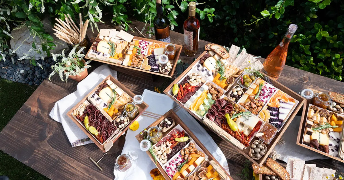 Creative charcuterie display with multiple themed boards and wine on a rustic outdoor table for a festive gathering