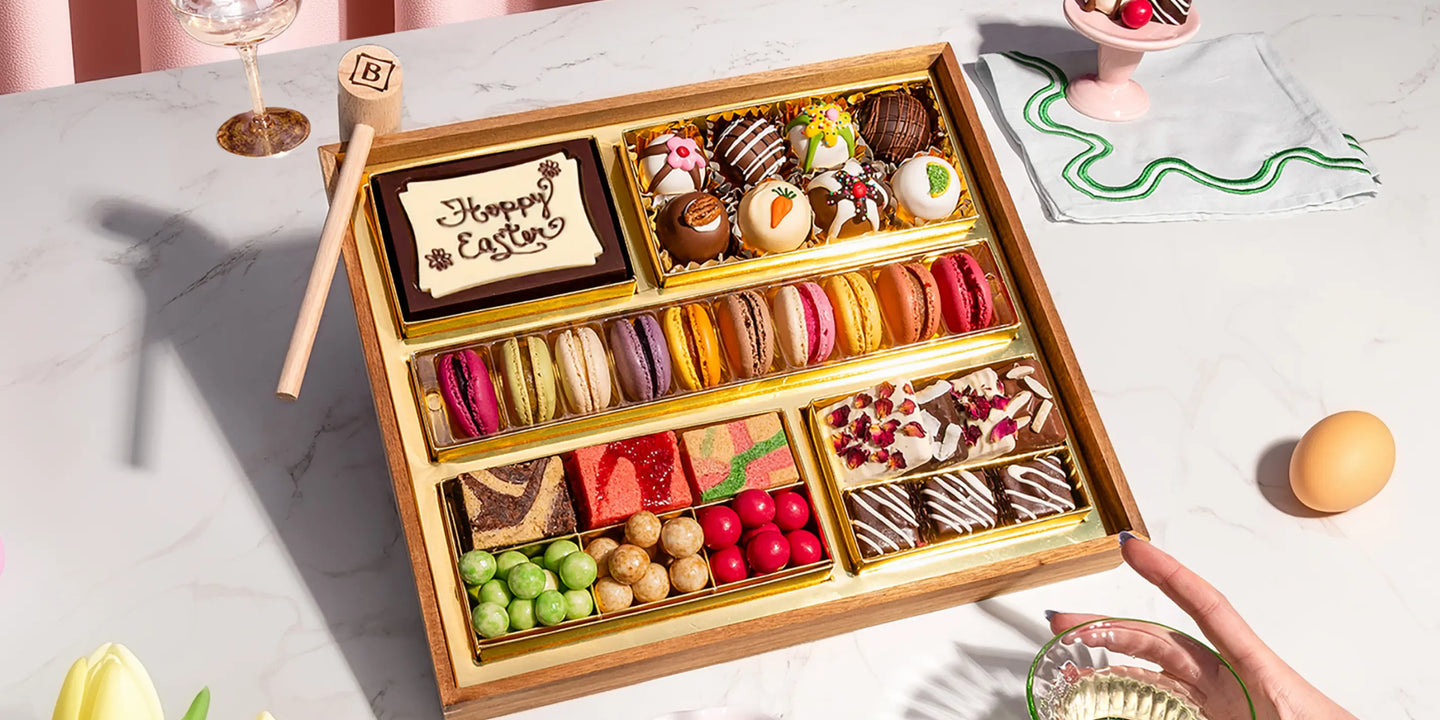 dessert grazing platter with macarons, decorated truffles, brownies, and candies in a gold-lined Easter tray on a marble surface