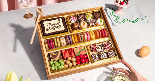 dessert grazing platter with macarons, decorated truffles, brownies, and candies in a gold-lined Easter tray on a marble surface