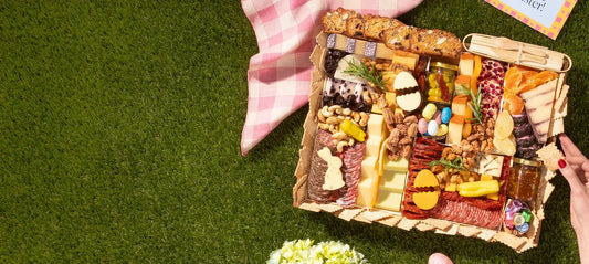 Summer charcuterie board arranged on grass with cheeses, colorful candies, nuts, and meats beside a picnic blanket.