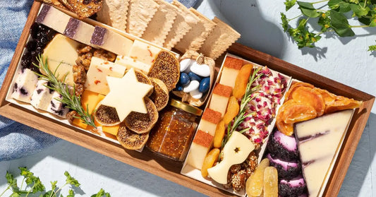 Festive cheese and meat board arranged with dried fruits, crackers, rosemary, and colorful cheeses in a wooden box