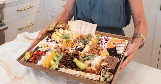 Gourmet charcuterie board featuring assorted cheeses, meats, fruits, nuts, crackers, and garnishes on a wooden tray