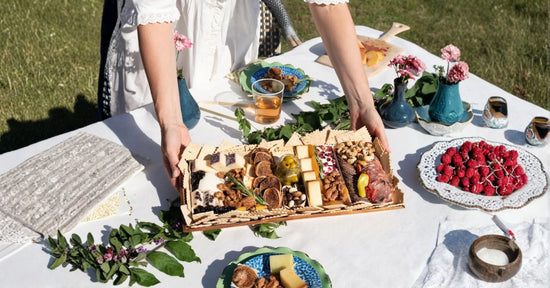 Charcuterie board with gourmet cheese, meats, figs, olives, and crackers hosted outdoors on a white linen-draped table with fresh flowers.