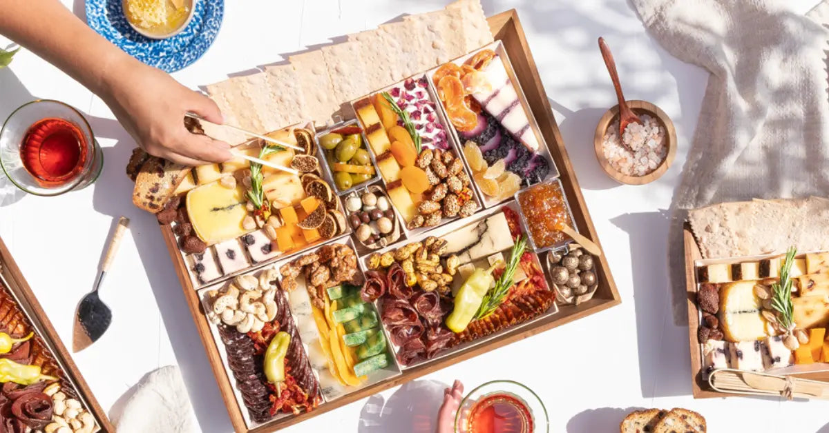 Salami and cheese board with nuts, dried fruit, olives, and spreads being served at a sunlit outdoor gathering