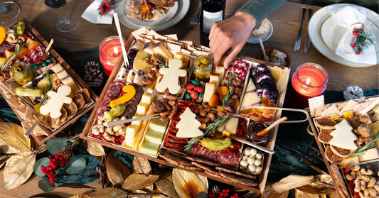 salty cured meats with cheddar and tree-shaped cheese on holiday boards with candles, pine cones, and red berries on a Christmas table