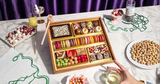 sweet grazing board ideas styled party spread with a dessert tray, small bowls of candy, drinks, and dessert accents on a marble surface