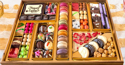 trendy dessert ideas in a large Easter board with macarons, truffles, chocolate bark, and colorful candies in a gold-lined wooden tray