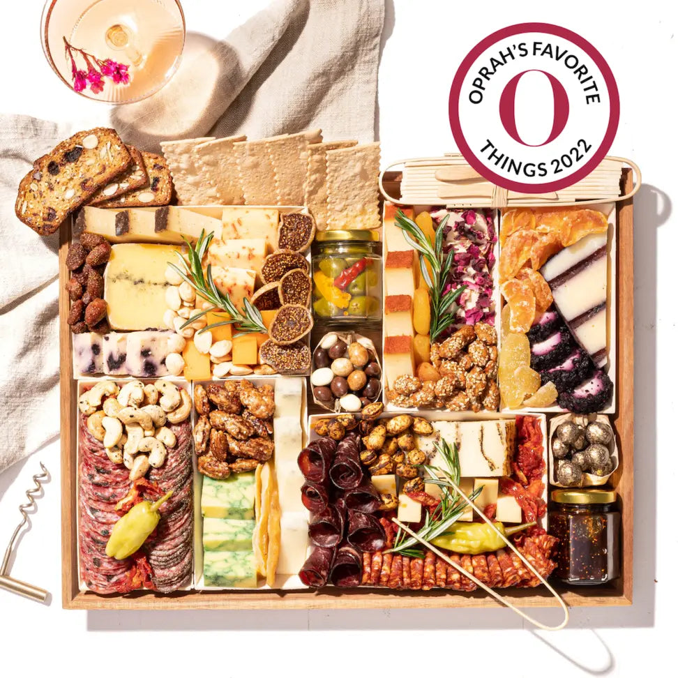 Oprah's Favorite Things 2022 charcuterie board featuring assorted cheeses, meats, nuts, dried fruits, and crackers with a cocktail on the side.