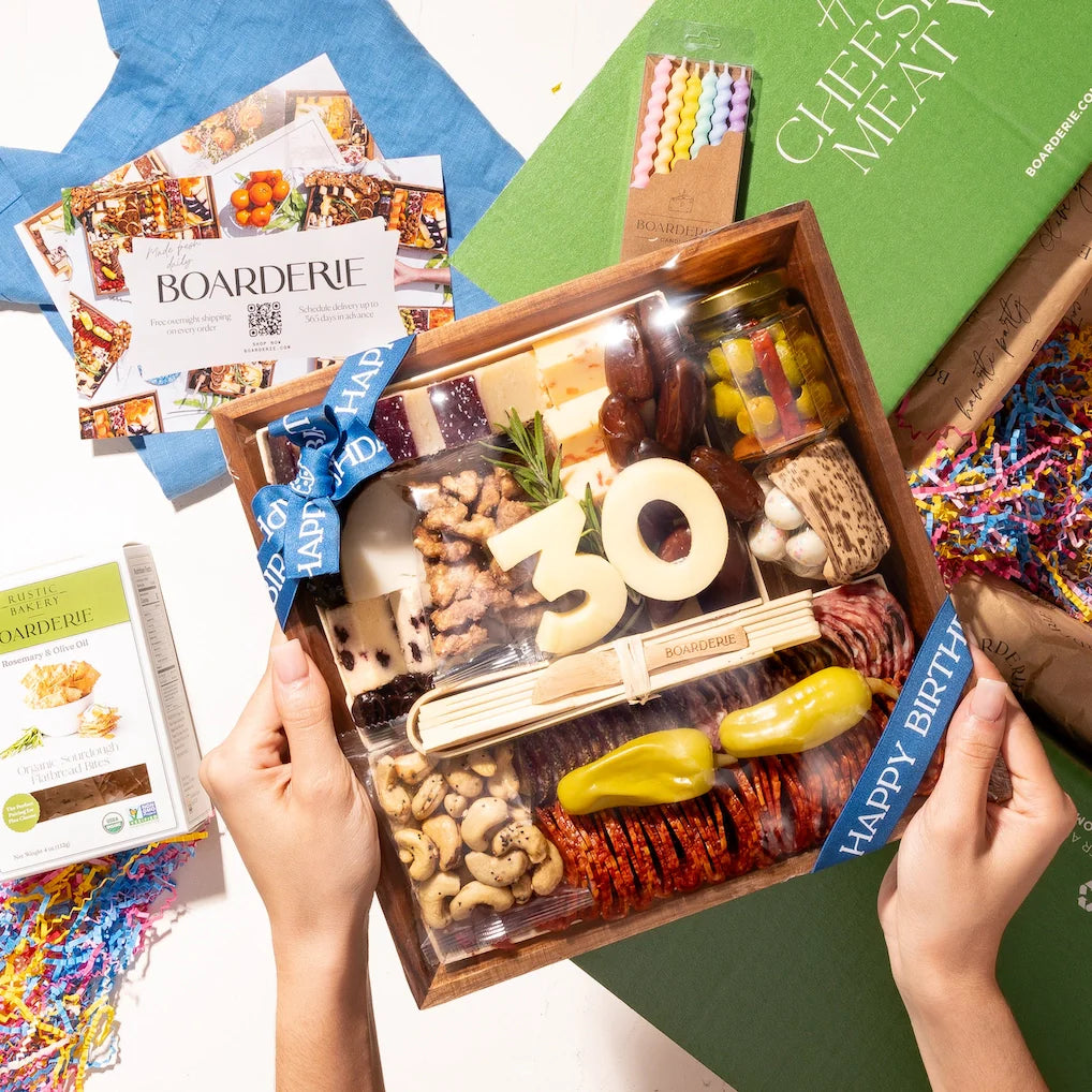Birthday-themed charcuterie board with cheese numbers "30," meats, nuts, and crackers, surrounded by confetti and festive candles.