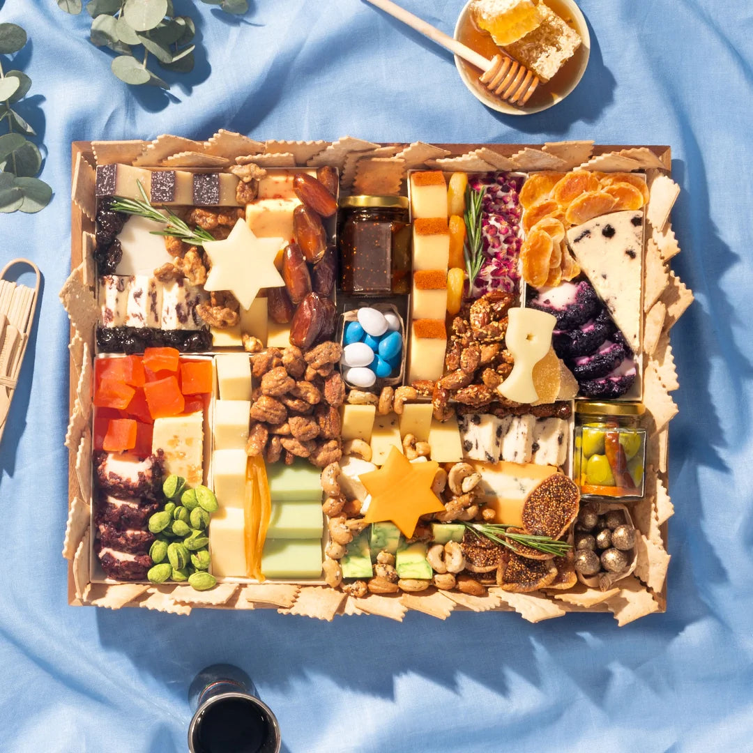 Hanukkah cheese board with Star of David cheese cutouts, dried fruit, nuts, olives, and honey on a blue cloth.
