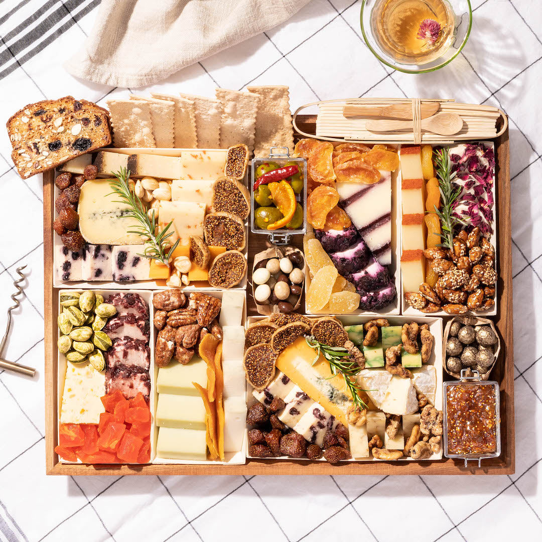 Elegant charcuterie board with an assortment of cheeses, nuts, dried fruits, crackers, and jam, set on a checkered tablecloth.