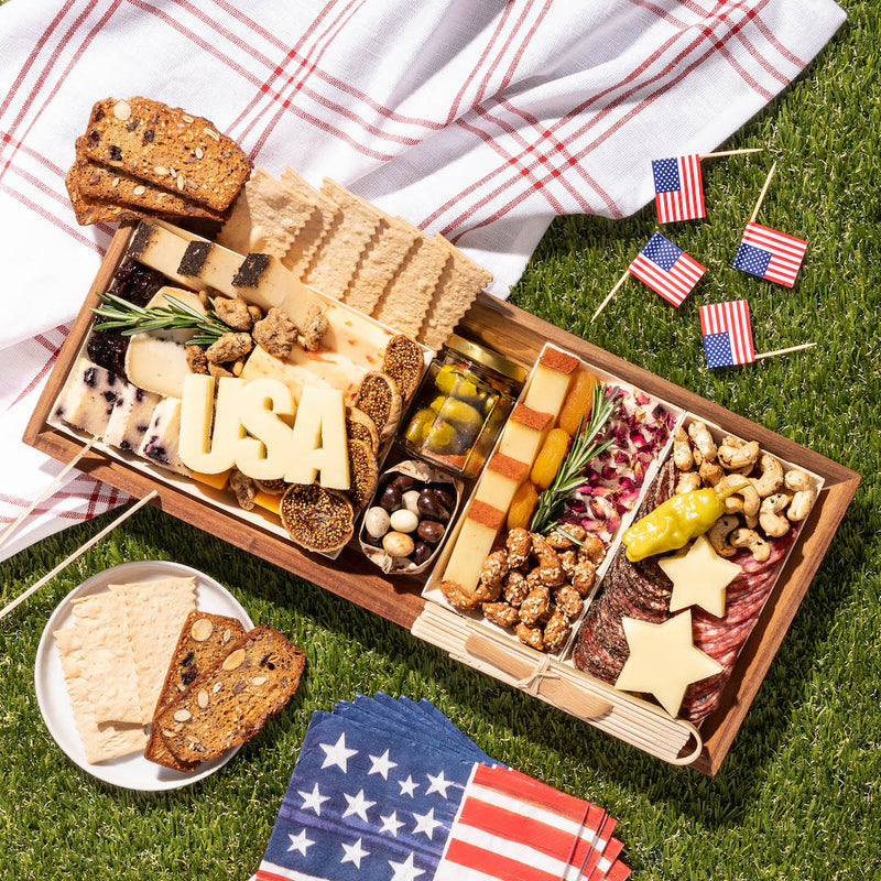 Independence Day charcuterie board featuring cheeses, meats, crackers, & star-shaped cheese slices, decorated with American flags