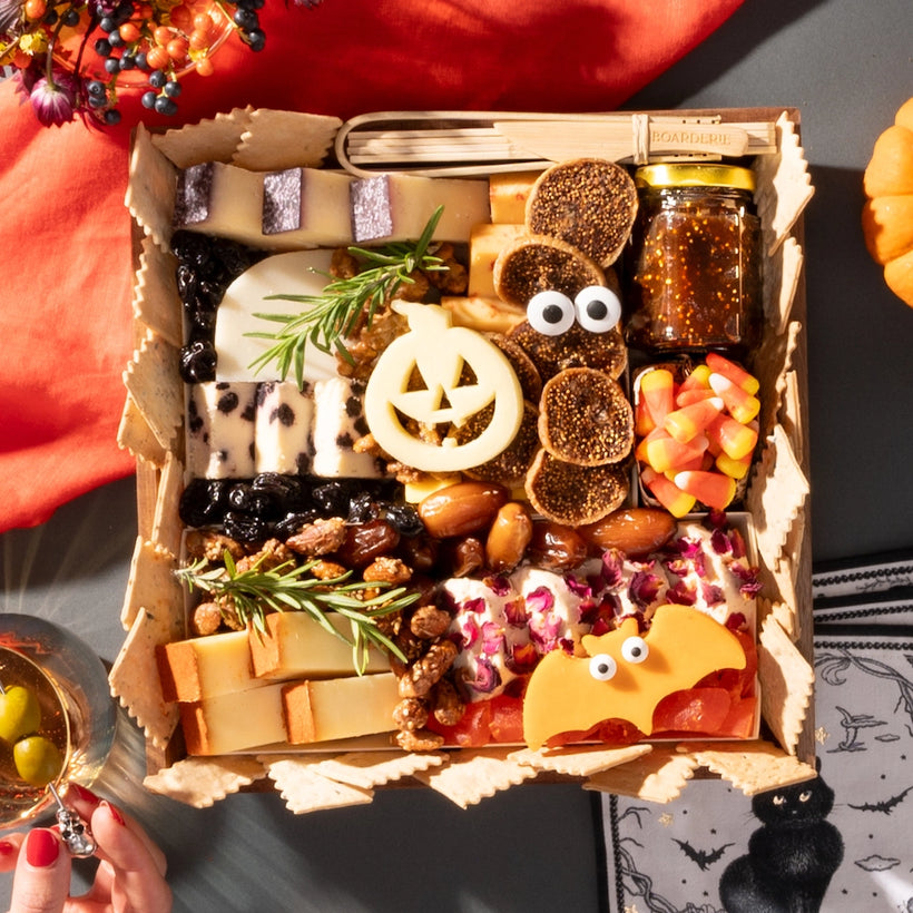 Halloween-themed cheese board with festive cheese shapes, figs, candy corn, nuts, and a small jar of fig jam, arranged without any meats