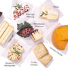 Assorted gourmet cheeses including Goat Fig & Rose Log, Wine Bathed Ubriacone, Truffle Cheddar, & Caraway Cheddar arranged on parchment paper