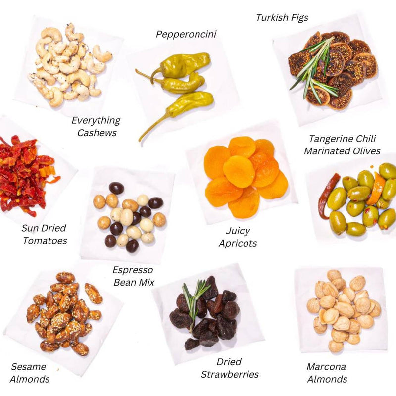 An assortment of gourmet snacks including everything cashews, pepperoncini, Turkish figs, tangerine chili marinated olives, juicy apricots, sun dried tomatoes, espresso bean mix, sesame almonds, dried strawberries, and Marcona almonds.