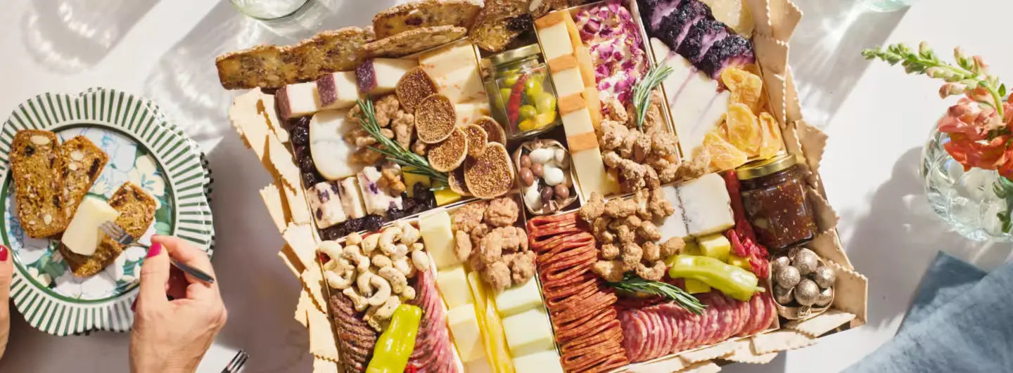 Large charcuterie board with assorted cheeses, meats, dried fruits, and nuts, served alongside crackers on decorative plates.