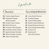 An ingredients list graphic with two columns titled 'Cheeses' and 'Accompaniments' on a light beige background. The cheeses listed include creamy aged gouda, peppadew pepper white cheddar, double cream gouda, merlot pecorino, cranberry wensleydale, apple smoked cheddar, white cheddar pumpkin, yellow cheddar bat, candied papaya, sweet sesame almonds, Turkish pitted dates, fig and orange marmalade, candy corn, and rosemary & olive oil crackers.